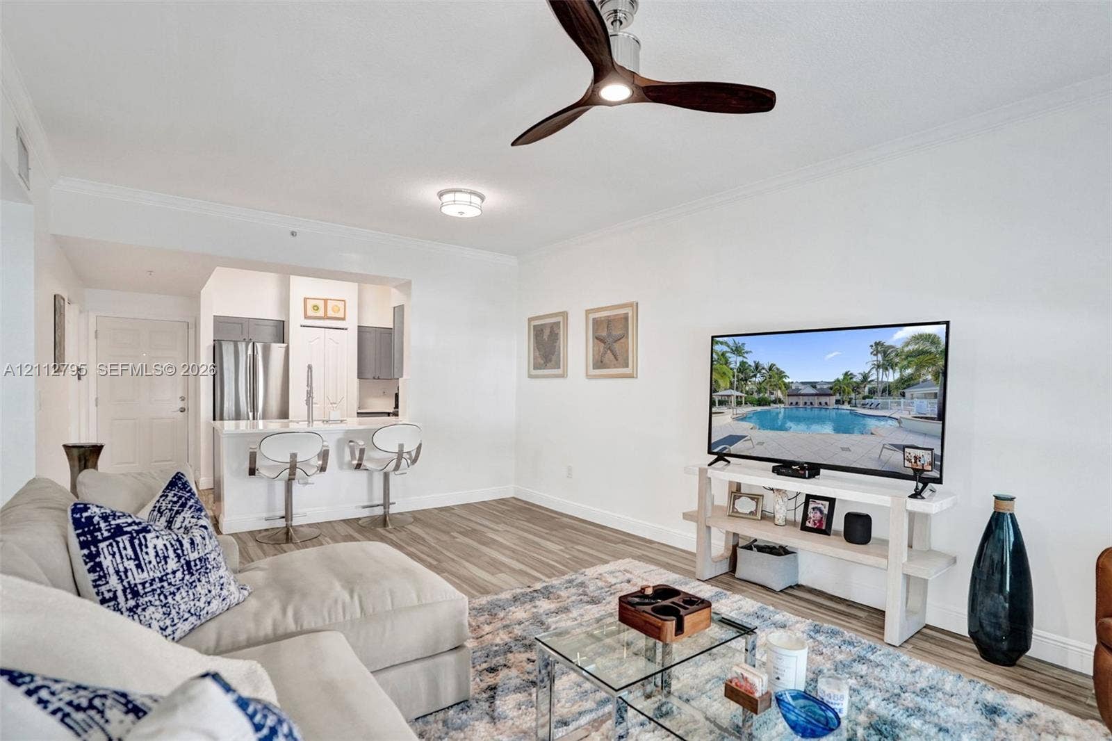 275 Murcia Drive, #205, Jupiter, FL 33458 Open-concept living space featuring wood-finish flooring, a modern three-blade ceiling fan, and a kitchen pass-through with a stone-surface breakfast bar