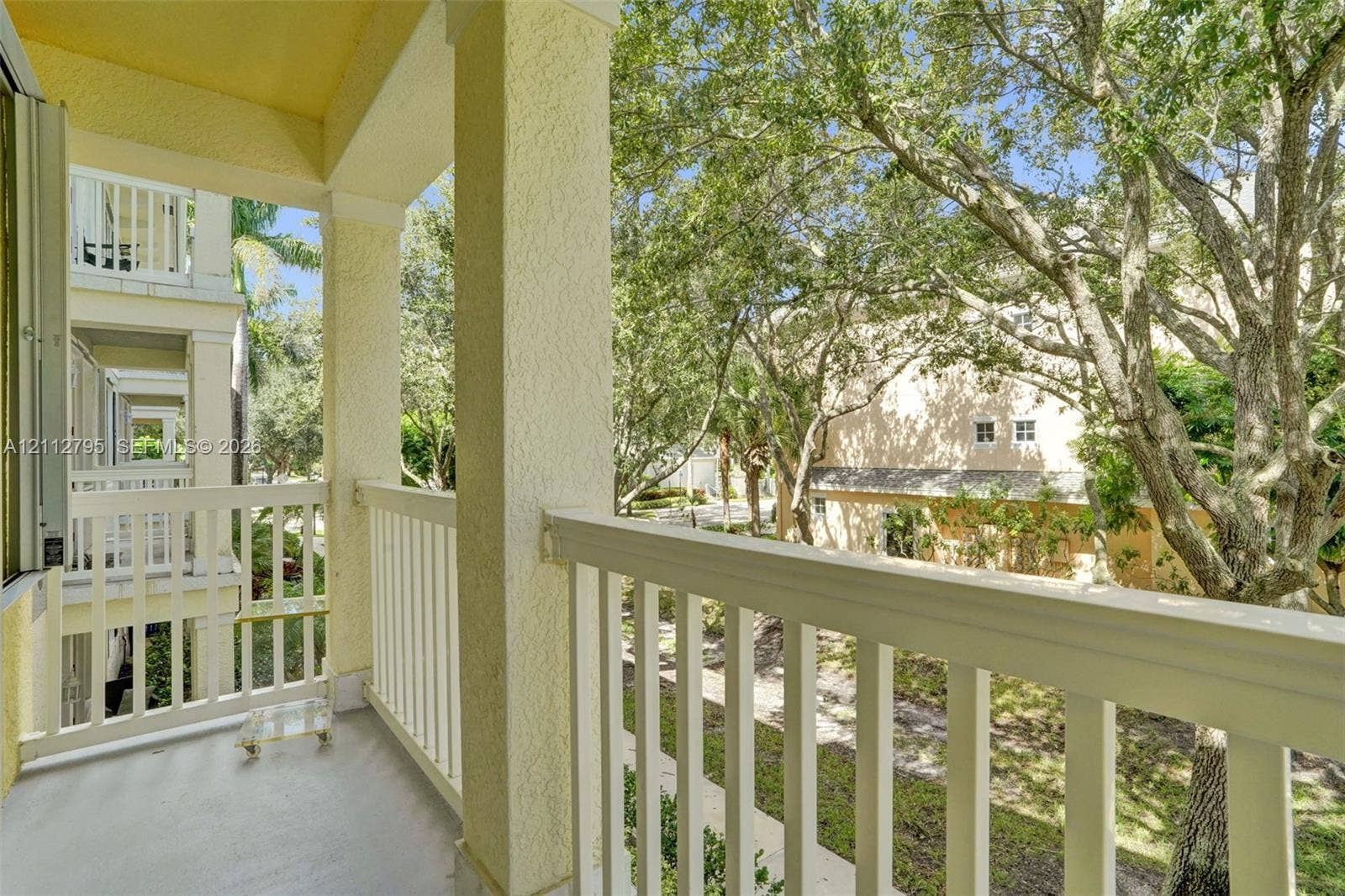 275 Murcia Drive, #205, Jupiter, FL 33458 Covered balcony featuring white vertical railings, stucco-finished support columns, and mature canopy trees