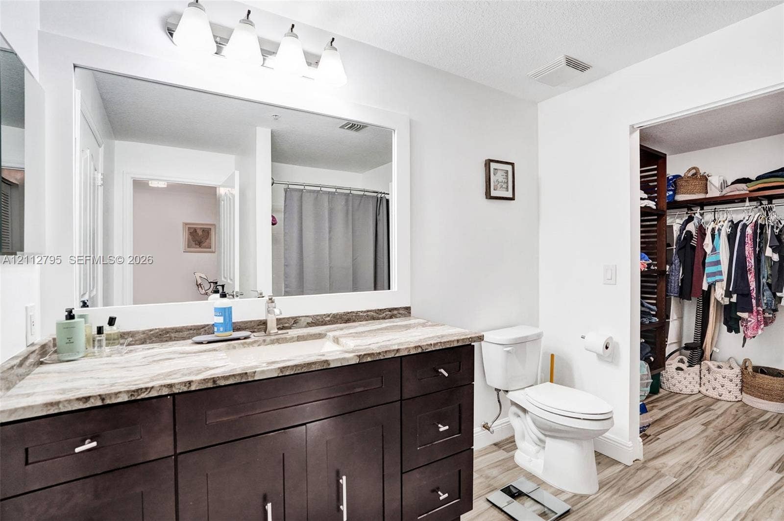 275 Murcia Drive, #205, Jupiter, FL 33458 Bathroom featuring a dark-finish vanity with stone-patterned countertop, large wall-mounted mirror, overhead multi-light fixture, and wood-finish flooring