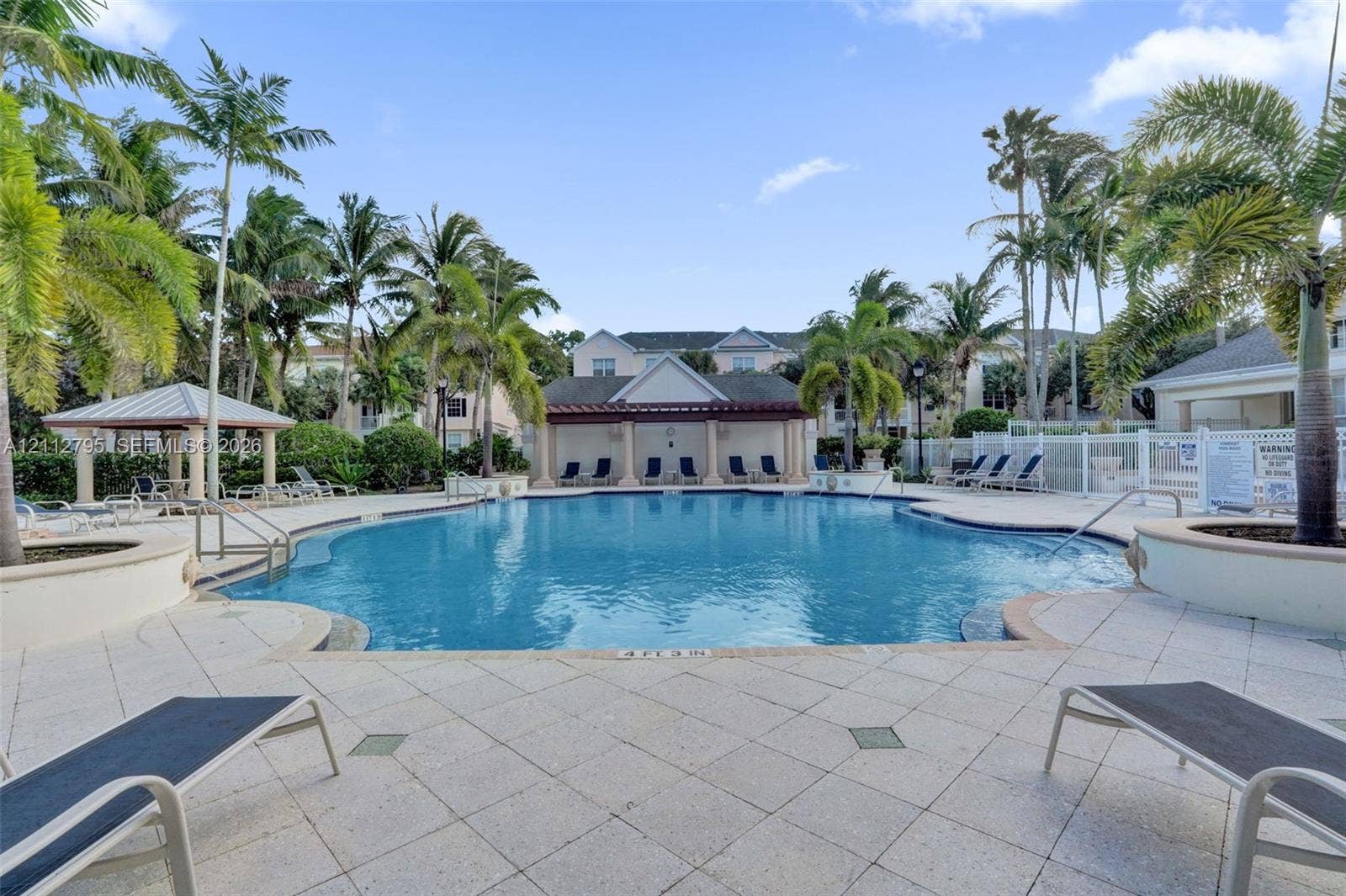 275 Murcia Drive, #205, Jupiter, FL 33458 Large community swimming pool featuring a stone-paver deck, multiple integrated spas, a covered cabana with columns, and mature palm trees