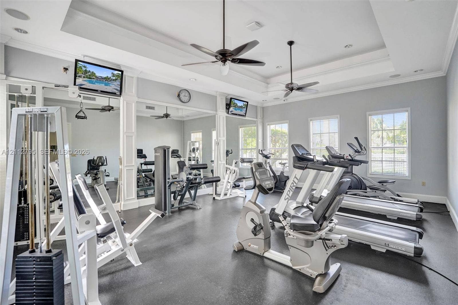 275 Murcia Drive, #205, Jupiter, FL 33458 Fitness room featuring tray ceilings, full-wall mirrors, multi-blade ceiling fans, and rubber flooring