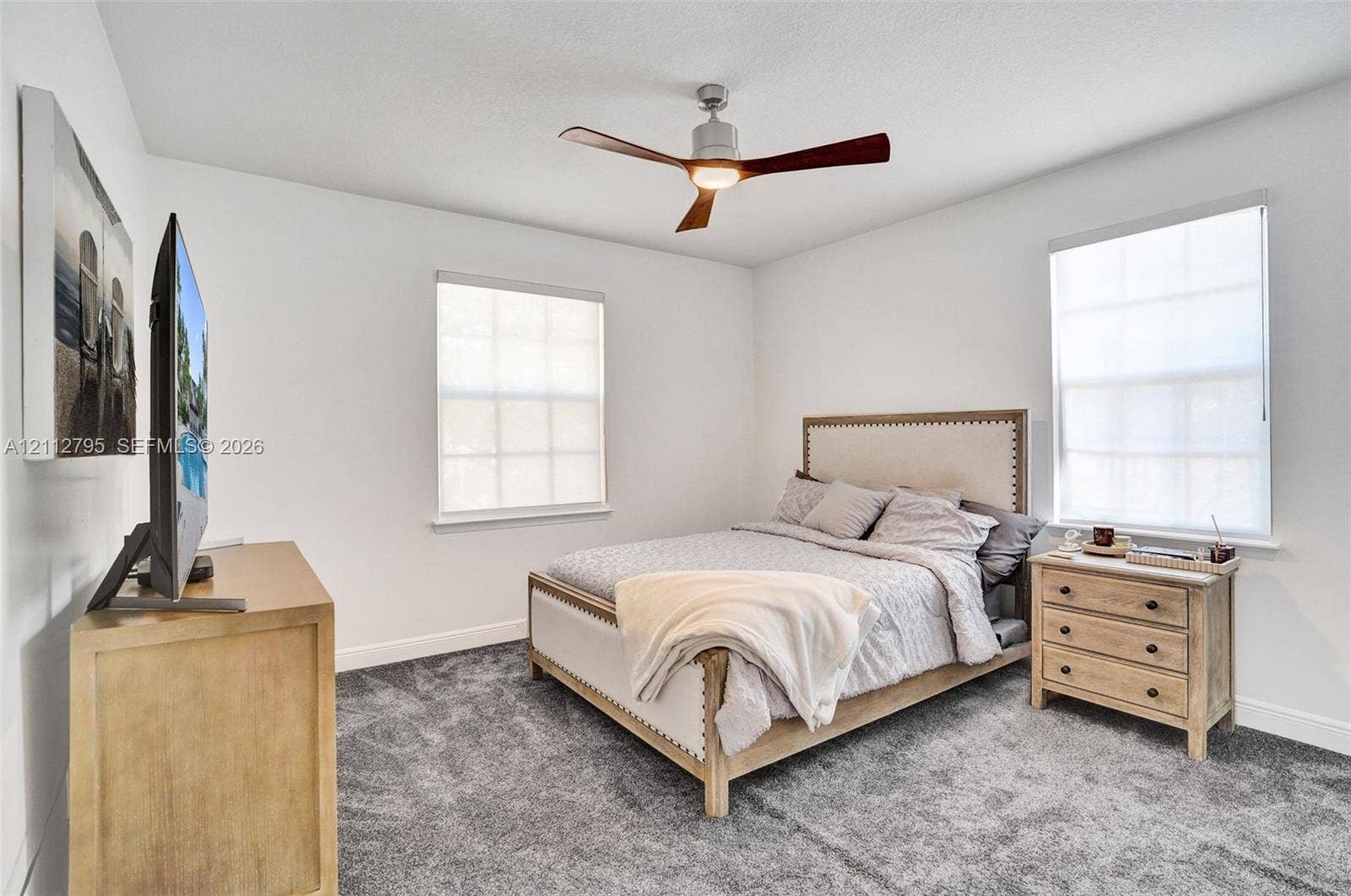 275 Murcia Drive, #205, Jupiter, FL 33458 Neutral-toned room featuring grey wall-to-wall carpeting, dual windows with roller shades, and a ceiling fan with integrated lighting
