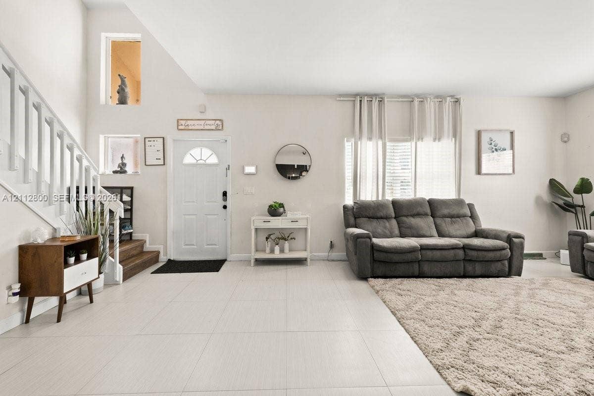 599 Racquet Club Road, #68-17, Weston, FL 33326 High-ceiling interior featuring tile flooring, a staircase with painted wood railings, multiple recessed wall niches, and a multi-paneled entry door