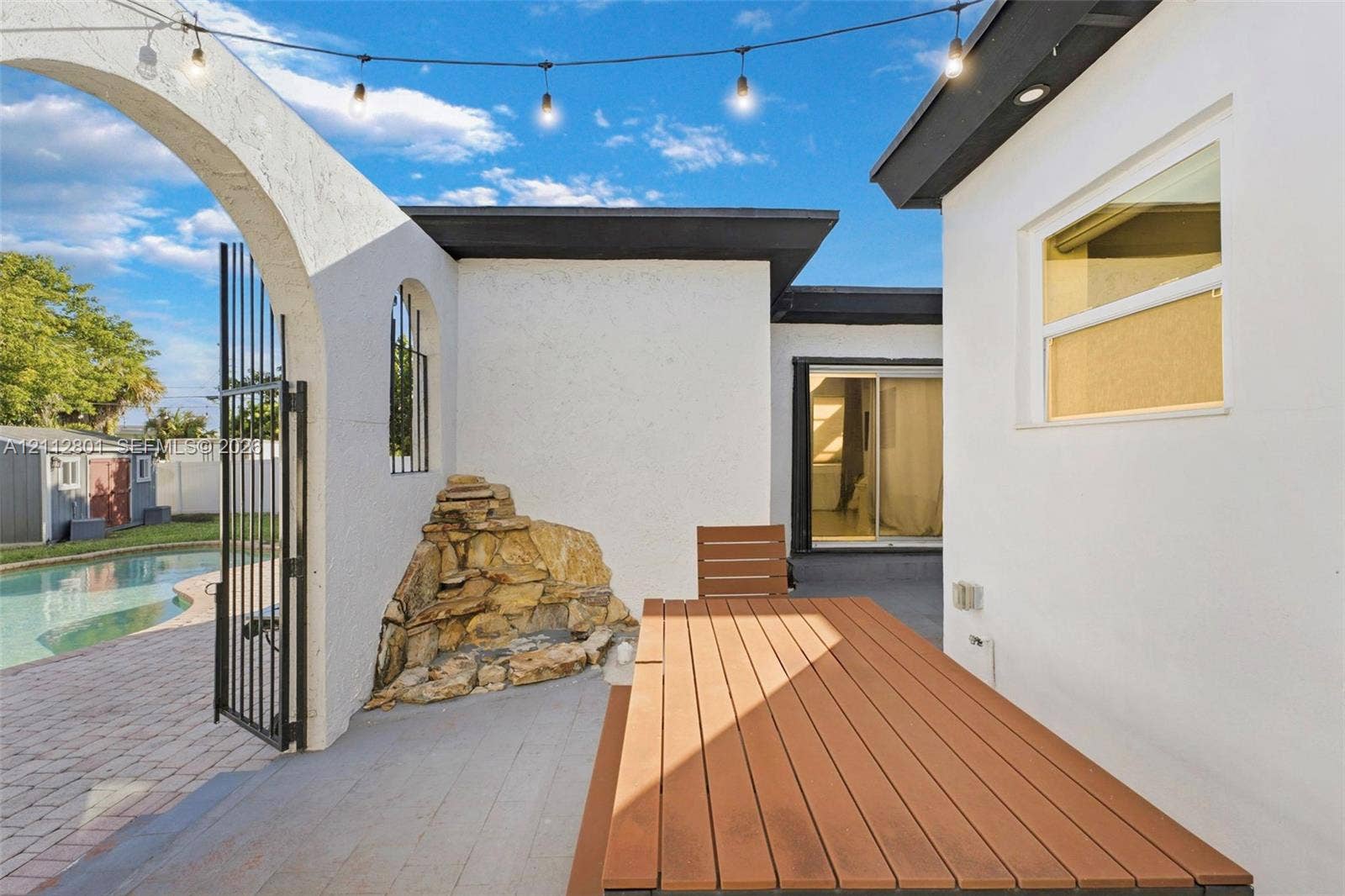 3241 SW 84th Court, Miami, FL 33155 Outdoor patio featuring a built-in stone water feature, decorative arched entryway, and integrated overhead string lighting