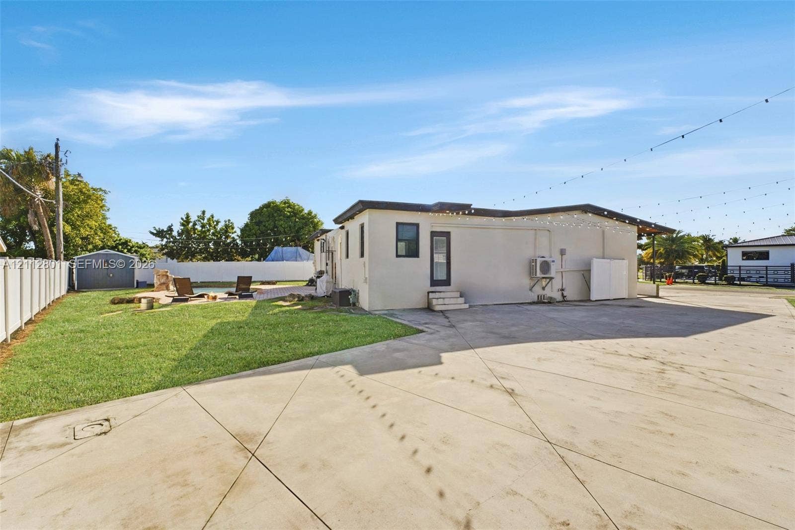 3241 SW 84th Court, Miami, FL 33155 Expansive concrete hardscaping, manicured lawn, white vinyl fencing, storage shed, and exterior string lighting