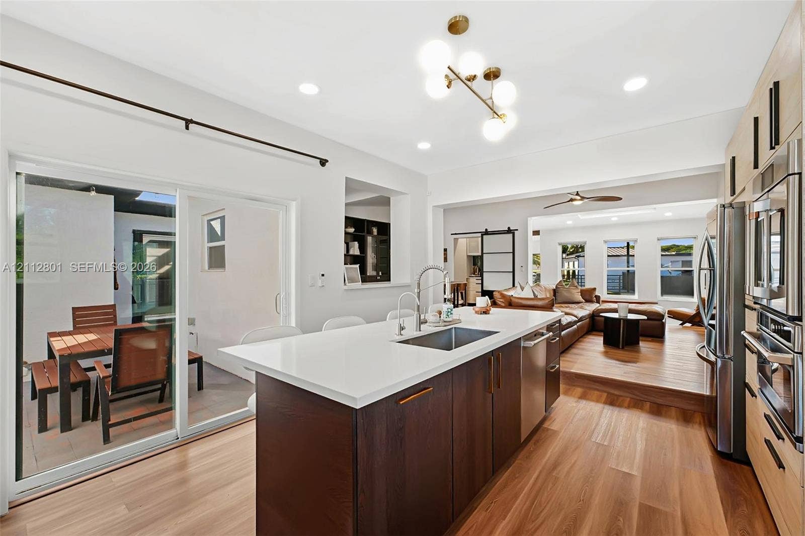 3241 SW 84th Court, Miami, FL 33155 Kitchen featuring a central island with a solid-surface countertop and undermount sink, dark-finish cabinetry, stainless steel appliances, wood-finish flooring, and a multi-globe light fixture