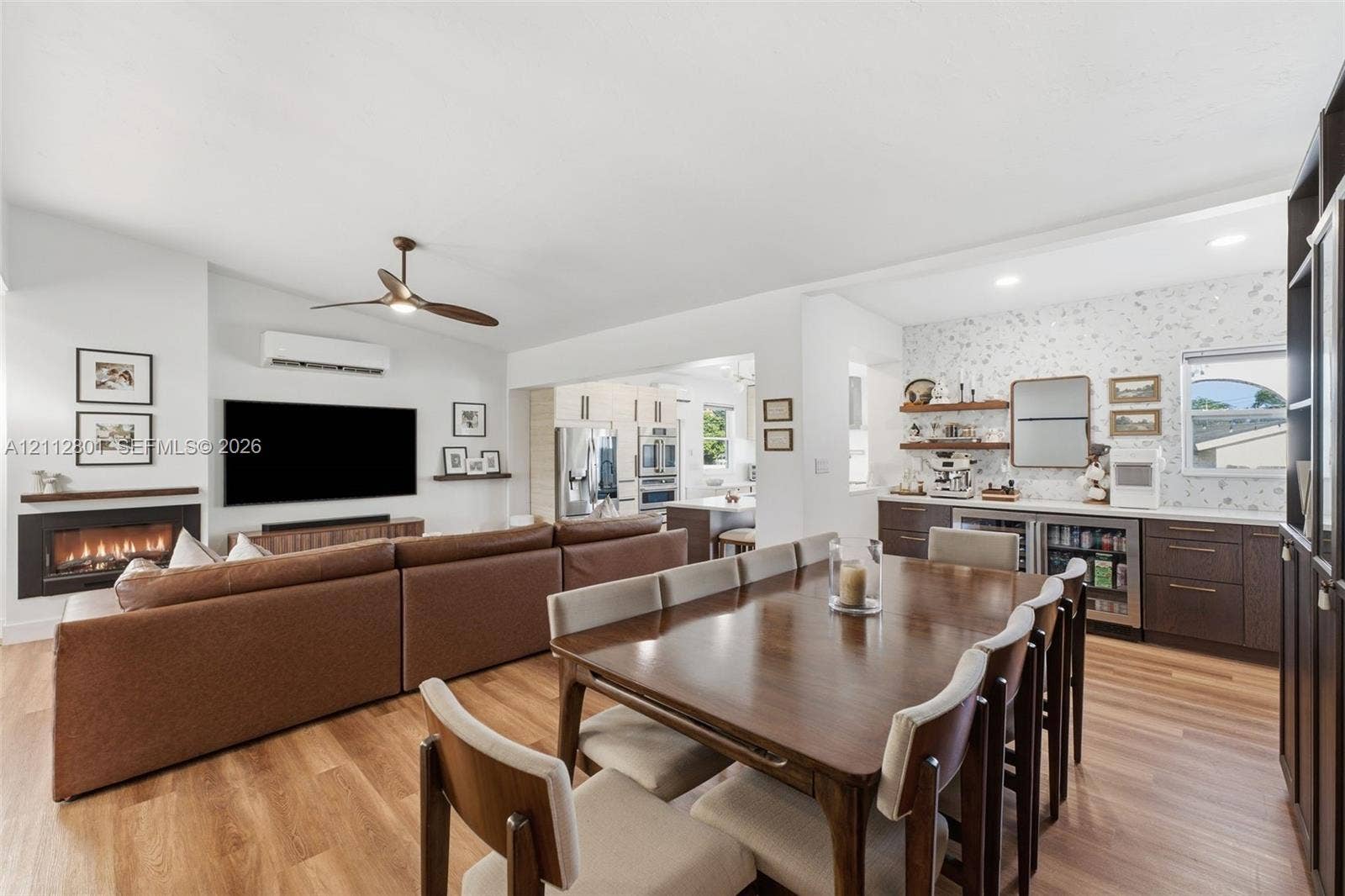 3241 SW 84th Court, Miami, FL 33155 Open-concept living space featuring wood-finish flooring, a wall-mounted linear fireplace with a floating mantel, a ceiling fan, recessed lighting, and a built-in wet bar with dark cabinetry