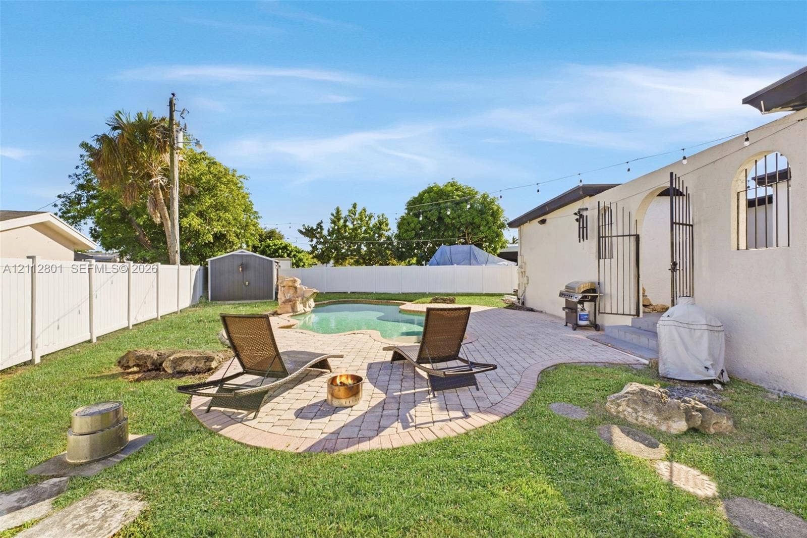 3241 SW 84th Court, Miami, FL 33155 Backyard featuring a freeform swimming pool, decorative stone accents, paver patio, and white vinyl perimeter fencing
