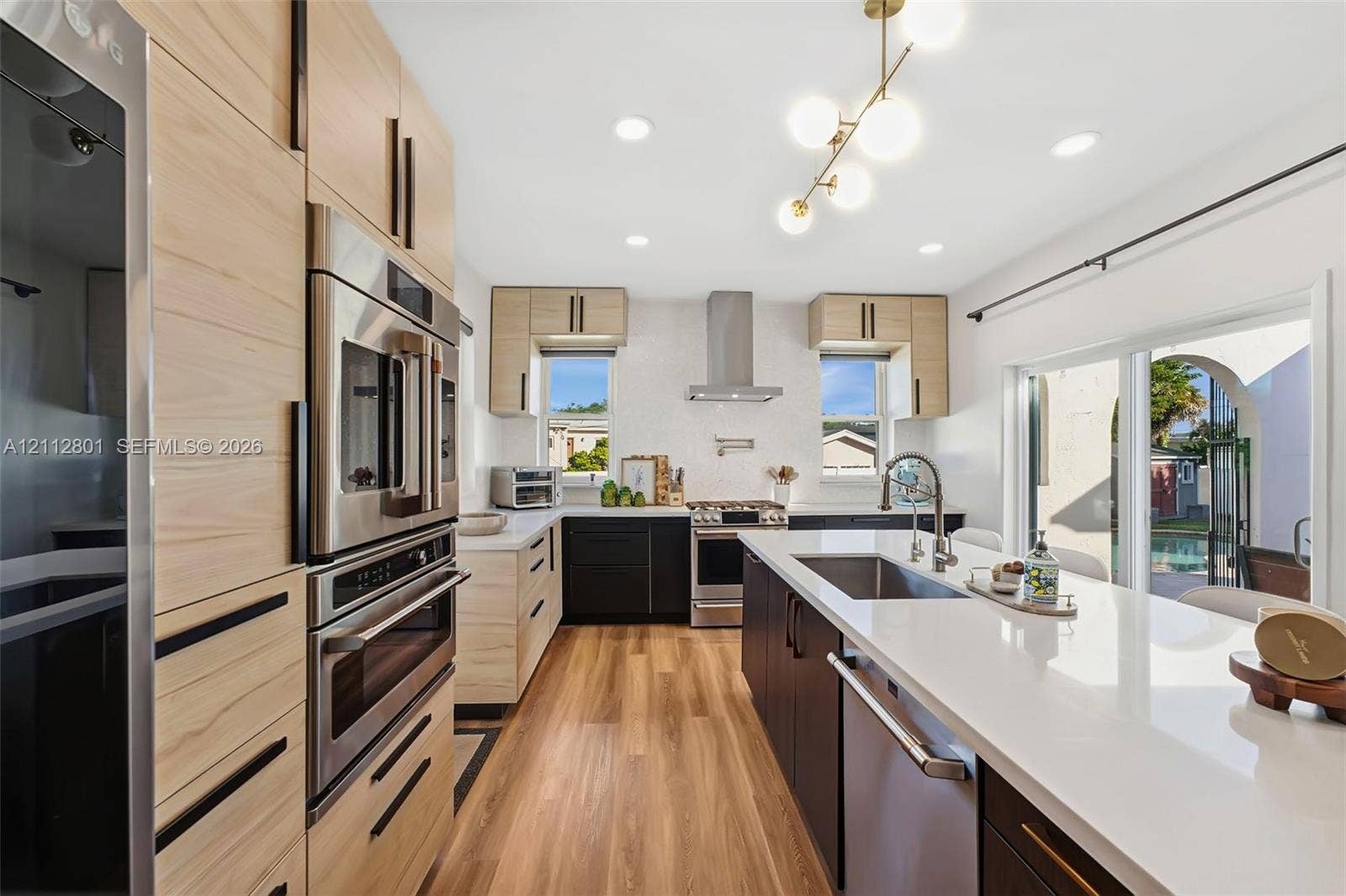 3241 SW 84th Court, Miami, FL 33155 Kitchen featuring two-tone cabinetry with wood-finish and matte black finishes, quartz countertops, stainless steel appliances, a center island with an undermount sink, and recessed lighting