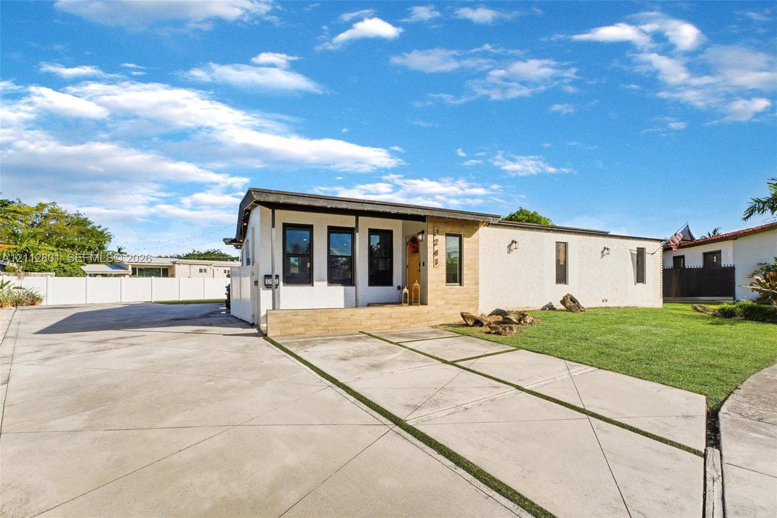 3241 SW 84th Court, Miami, FL 33155 Single-story exterior featuring a stone-accented facade, covered entryway, concrete driveway with integrated turf strips, and perimeter privacy fencing