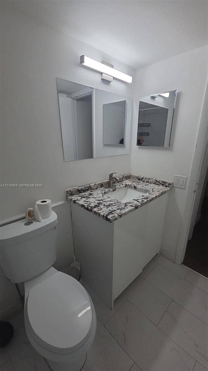 Vanity featuring a stone-patterned countertop, integrated basin, white cabinetry, wall-mounted rectangular vanity mirror, and linear LED lighting