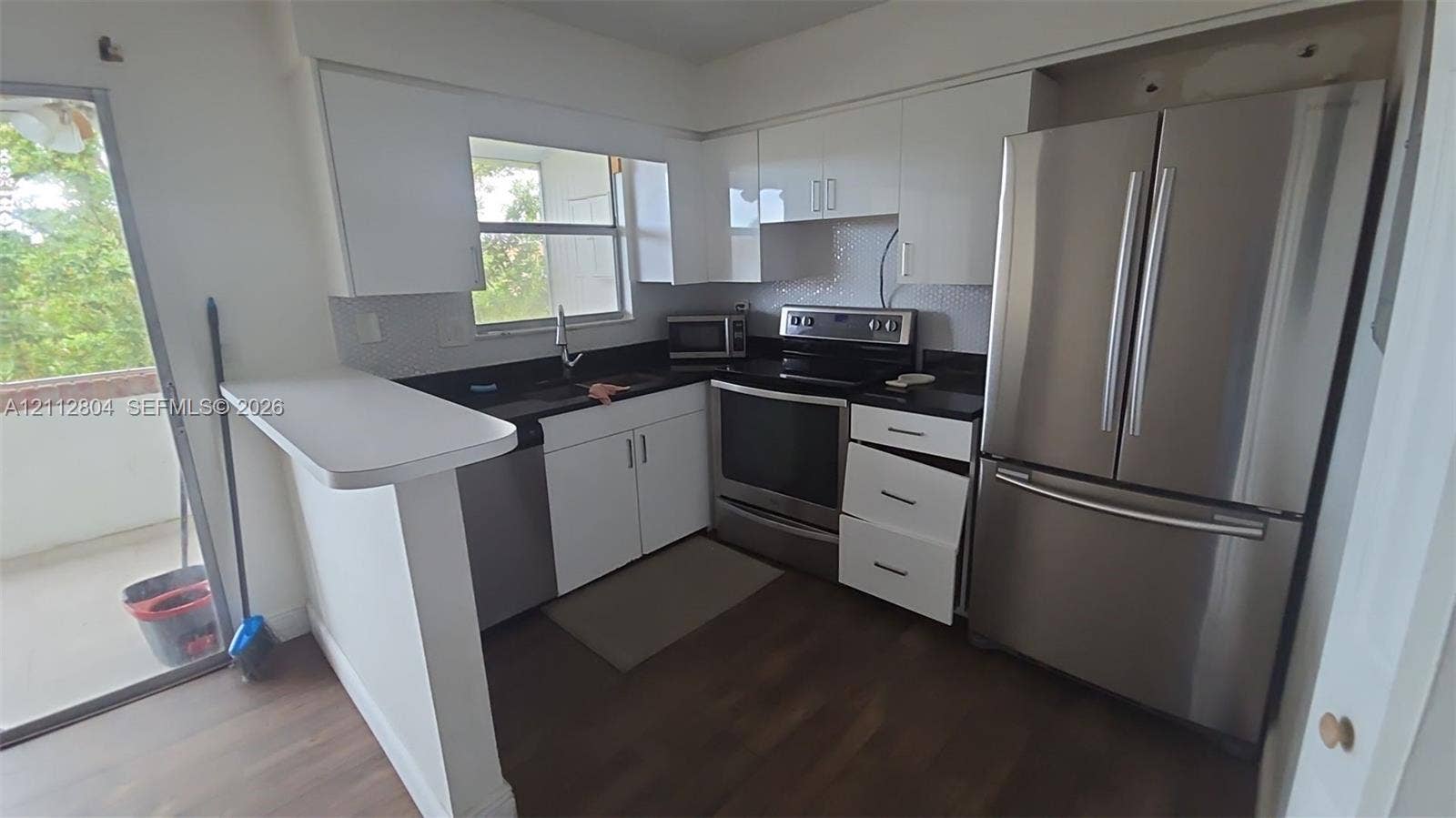 Kitchen featuring white cabinetry, dark countertops, wood-finish flooring, stainless steel appliances, and an integrated breakfast bar