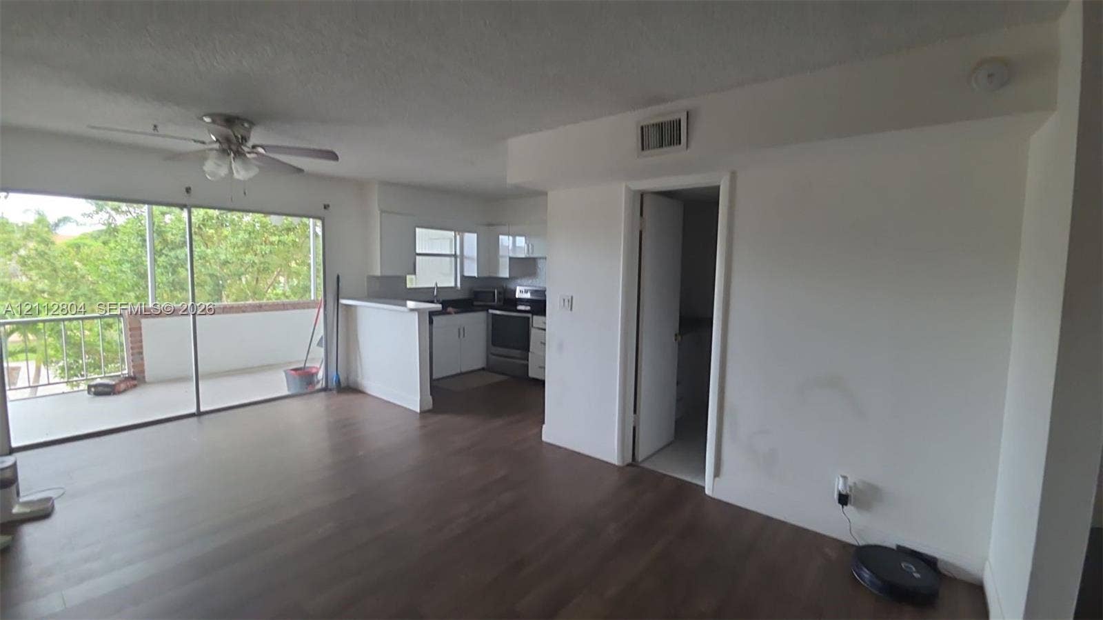 Open-concept area featuring wood-finish flooring, a kitchen with white cabinetry, stainless steel range, a breakfast bar, and large sliding glass doors opening to a balcony