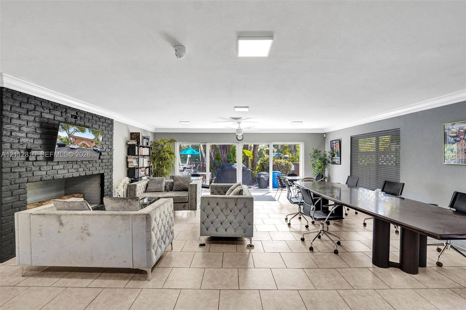 1920 NE 1st Terrace, #107H, Wilton Manors, FL 33305 Interior space featuring tile flooring, a floor-to-ceiling painted brick fireplace surround, crown molding, and glass sliding doors