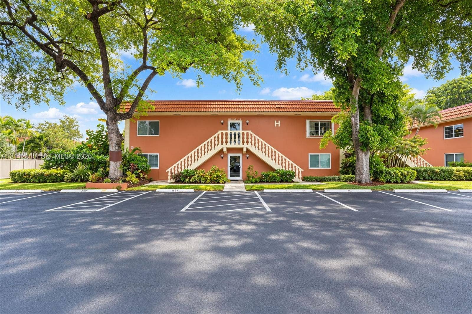 1920 NE 1st Terrace, #107H, Wilton Manors, FL 33305 Two-story exterior featuring a clay tile roof, stucco facade, external staircase with balustrade railings, and paved surface parking