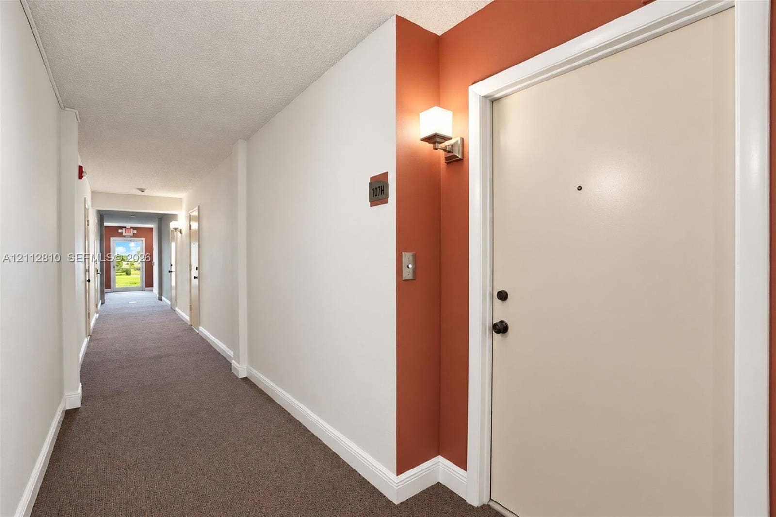 1920 NE 1st Terrace, #107H, Wilton Manors, FL 33305 Interior hallway featuring carpeting, accent wall paint, and wall-mounted lighting fixtures