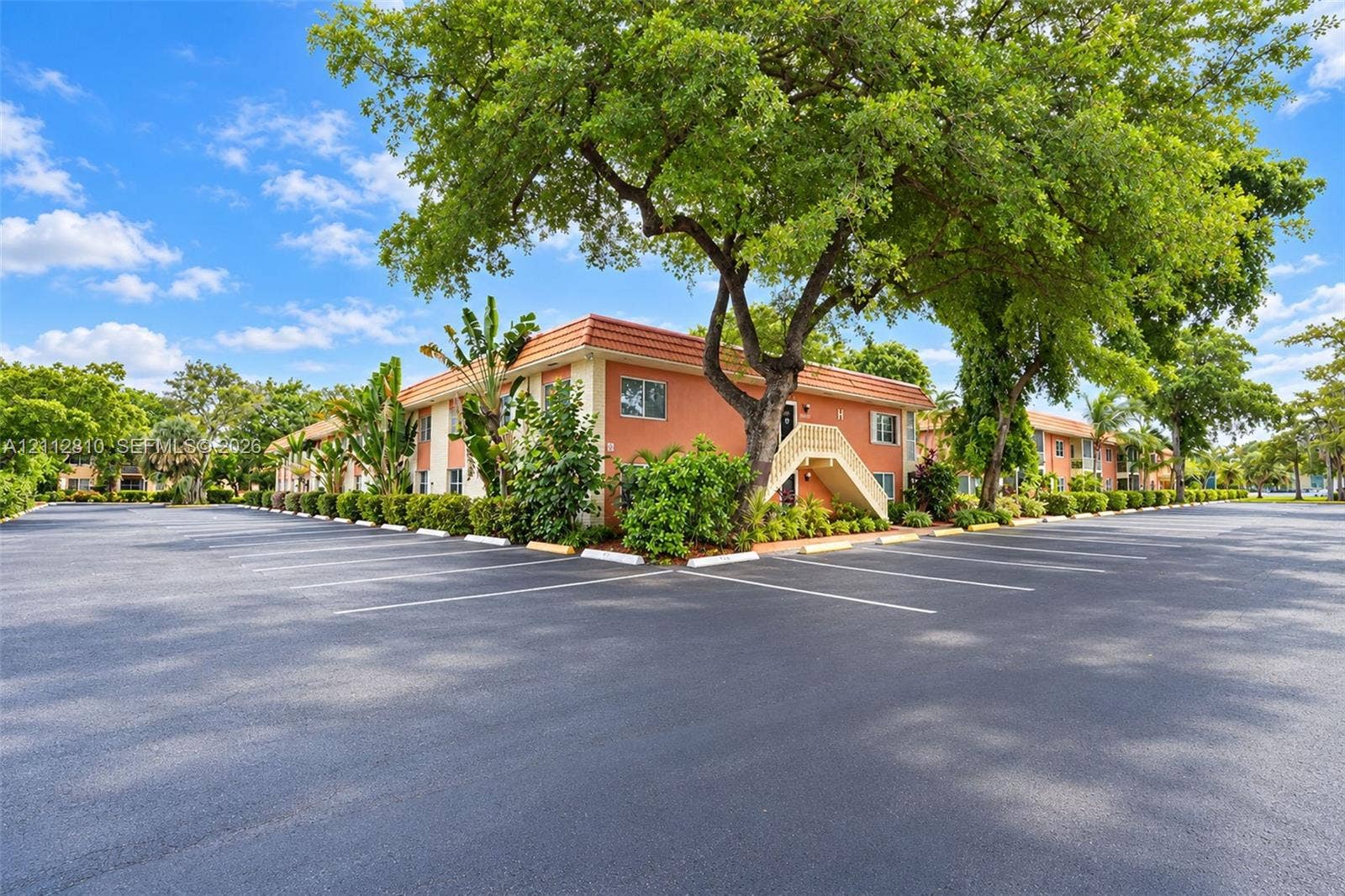 1920 NE 1st Terrace, #107H, Wilton Manors, FL 33305 Multi-story building featuring stucco exterior walls, a tile roof, paved parking area, and mature landscaping
