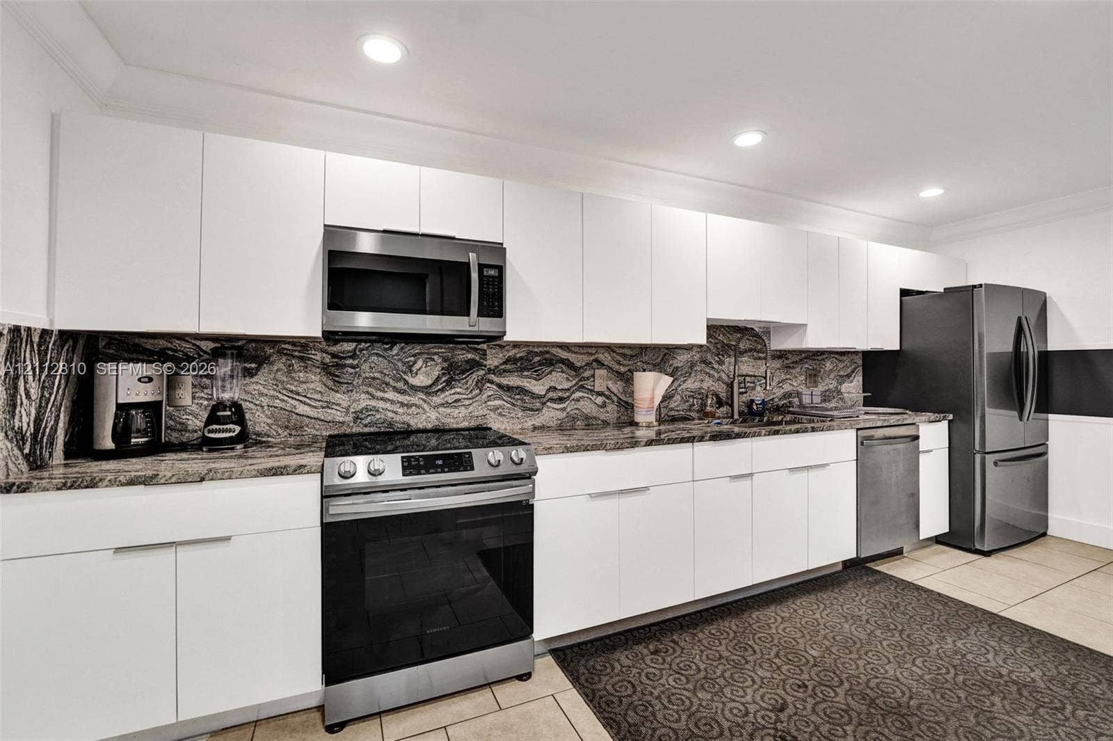 1920 NE 1st Terrace, #107H, Wilton Manors, FL 33305 Kitchen featuring flat-panel white cabinetry, stone slab backsplash, stainless steel appliances, and recessed lighting