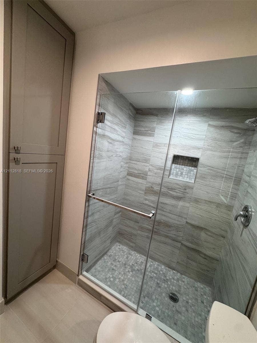 Walk-in shower featuring a frameless glass door, stone-tile flooring, horizontal wall tiling, an integrated recessed niche, and tall built-in cabinetry
