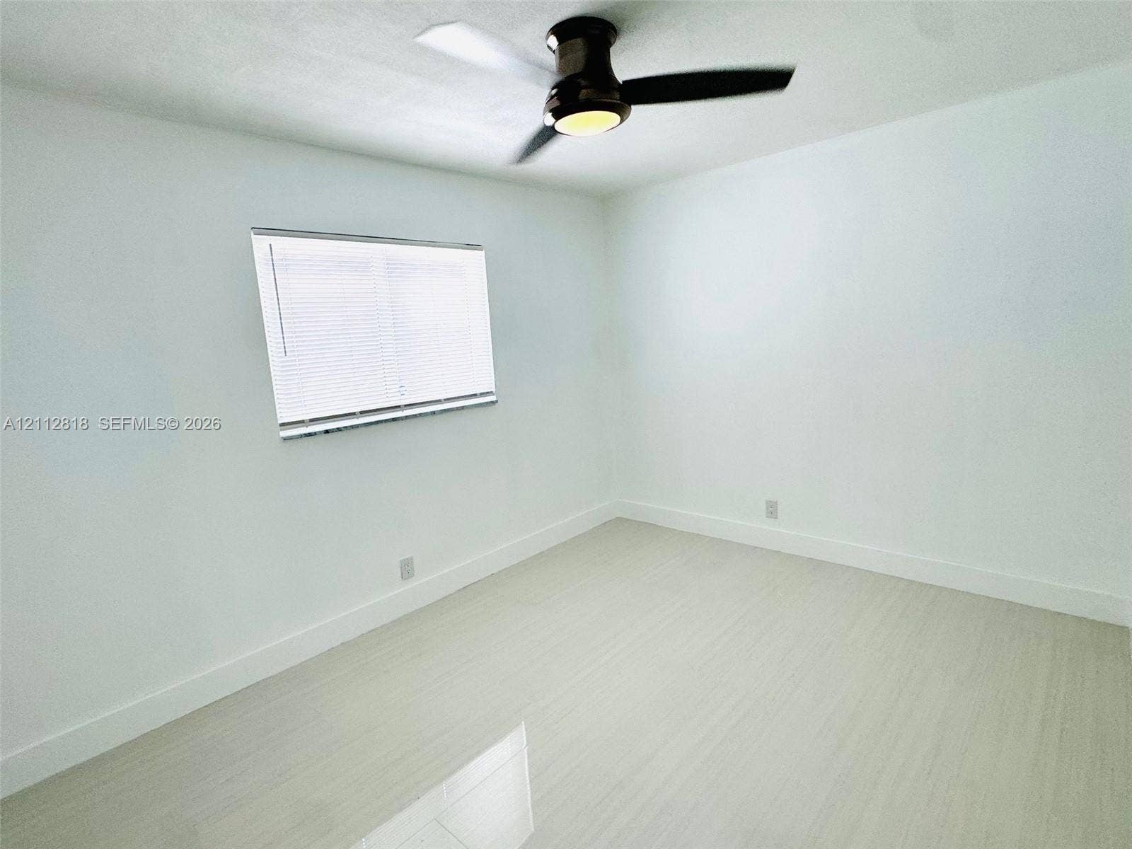 Interior room featuring light-toned wood-finish flooring, white walls, a dual-pane horizontal sliding window with blinds, and a matte black ceiling fan with an integrated light fixture