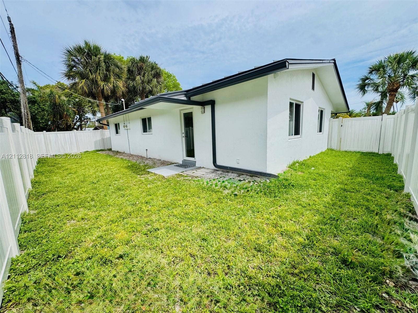 Exterior of the residence featuring white stucco siding, a low-pitch roofline, and white vinyl privacy fencing enclosing the perimeter of the lawn