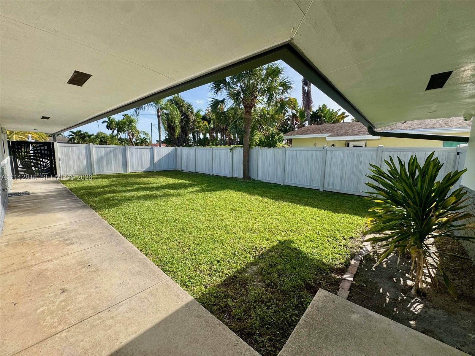 Covered concrete patio, fenced backyard, and established palm trees