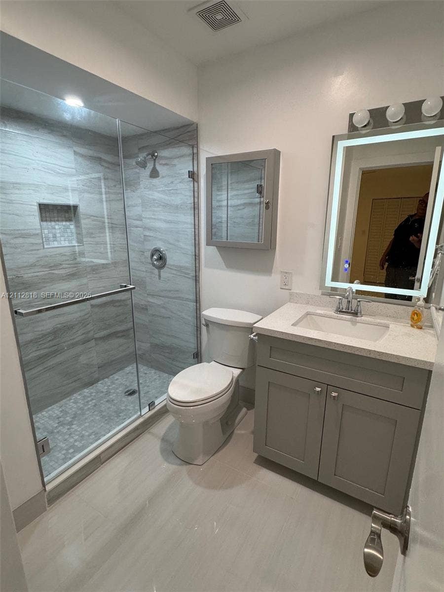 Bathroom featuring a walk-in shower with floor-to-ceiling tile, a built-in recessed niche, and a glass enclosure, paired with a vanity containing a quartz countertop, an integrated sink, and an LED-lit mirror
