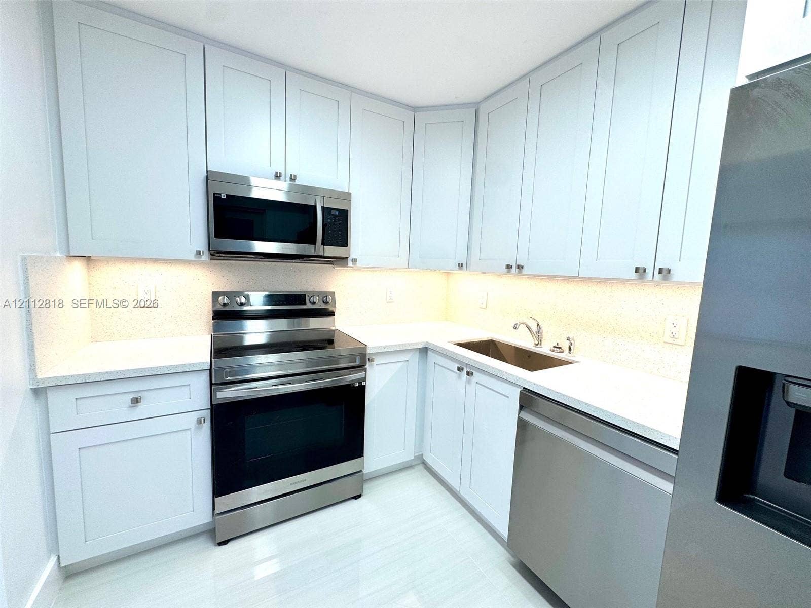Shaker-style cabinetry, stainless steel appliances, light-toned stone-finish countertops, under-cabinet lighting, and integrated sink