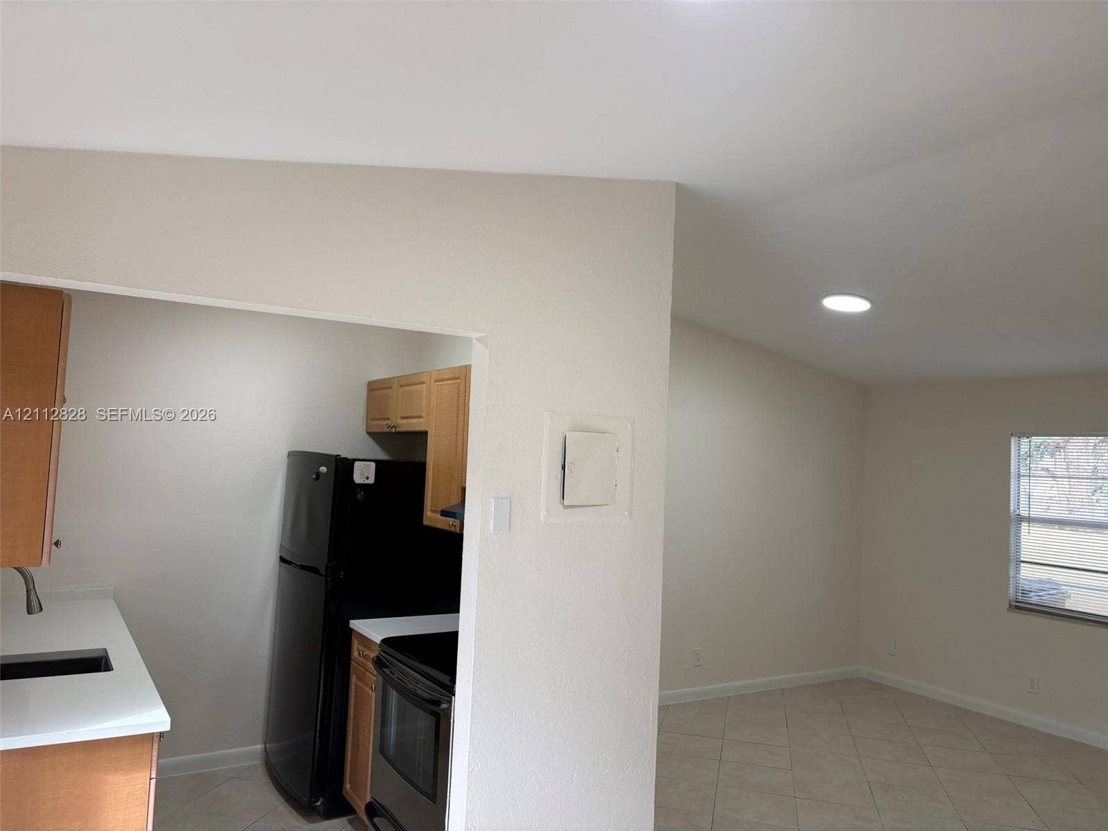 508 NW 43rd Place, Deerfield Beach, FL 33064 Kitchen featuring wood cabinetry, solid-surface countertops, and black appliances, paired with a room finished with tile flooring and recessed lighting