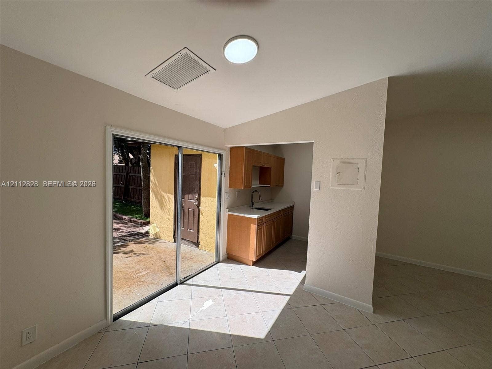 508 NW 43rd Place, Deerfield Beach, FL 33064 Sliding glass door, light-colored tile flooring, wood-finish cabinetry, countertop with a drop-in sink, and vaulted ceiling