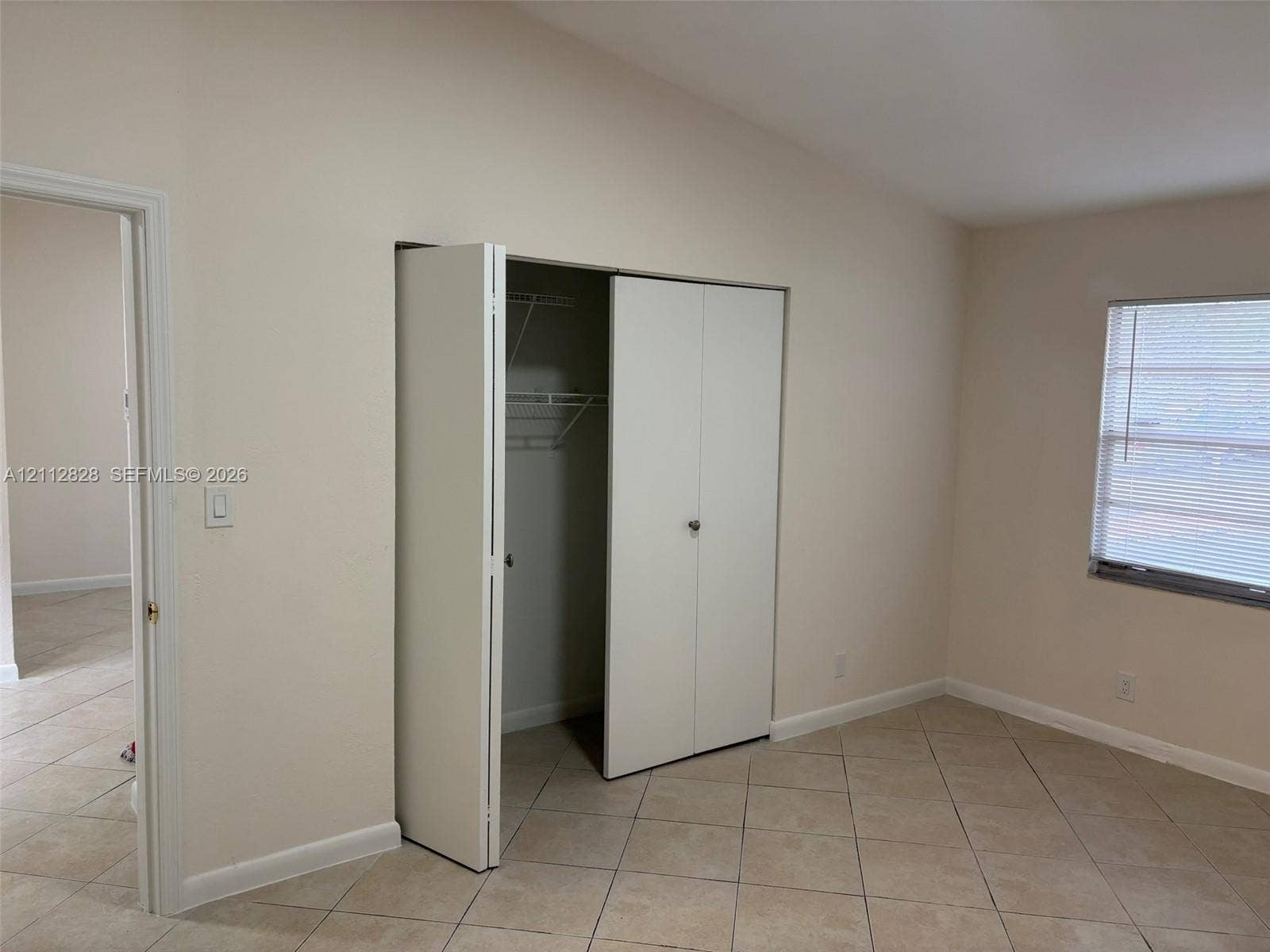 508 NW 43rd Place, Deerfield Beach, FL 33064 Interior room featuring neutral wall tones, large-format tile flooring, a closet with bifold doors and integrated shelving, and a window with horizontal blinds