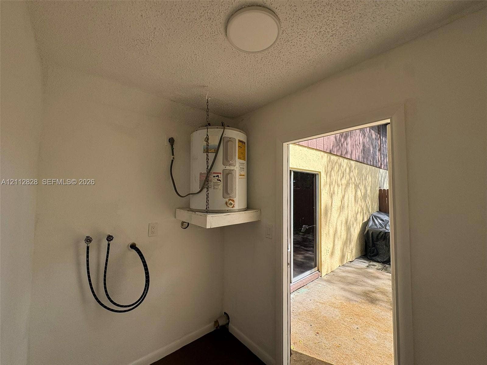 508 NW 43rd Place, Deerfield Beach, FL 33064 Utility space featuring a wall-mounted water heater, dedicated plumbing hookups, and a flush-mount ceiling light fixture, with access to an exterior concrete patio