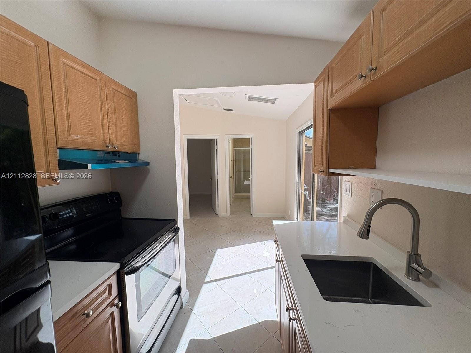 508 NW 43rd Place, Deerfield Beach, FL 33064 Kitchen featuring wood-finish cabinetry, white solid-surface countertops, a stainless steel undermount sink with a gooseneck faucet, and tile flooring