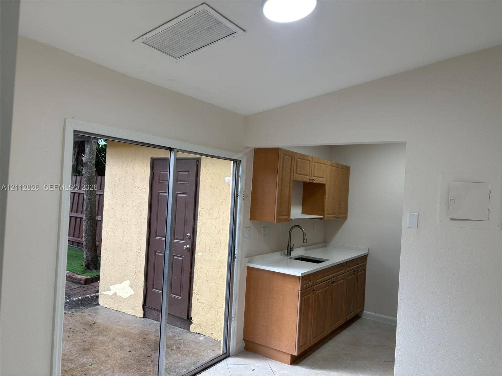 508 NW 43rd Place, Deerfield Beach, FL 33064 Kitchen featuring wood cabinetry, white countertops, and a stainless steel sink with a gooseneck faucet, accompanied by sliding glass doors opening to an exterior patio with a textured wall finish