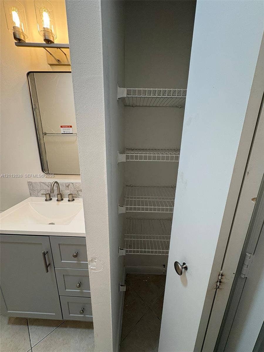 508 NW 43rd Place, Deerfield Beach, FL 33064 Vanity featuring grey shaker-style cabinetry, a solid-surface countertop with an integrated basin, a polished nickel widespread faucet, and a rectangular mirror