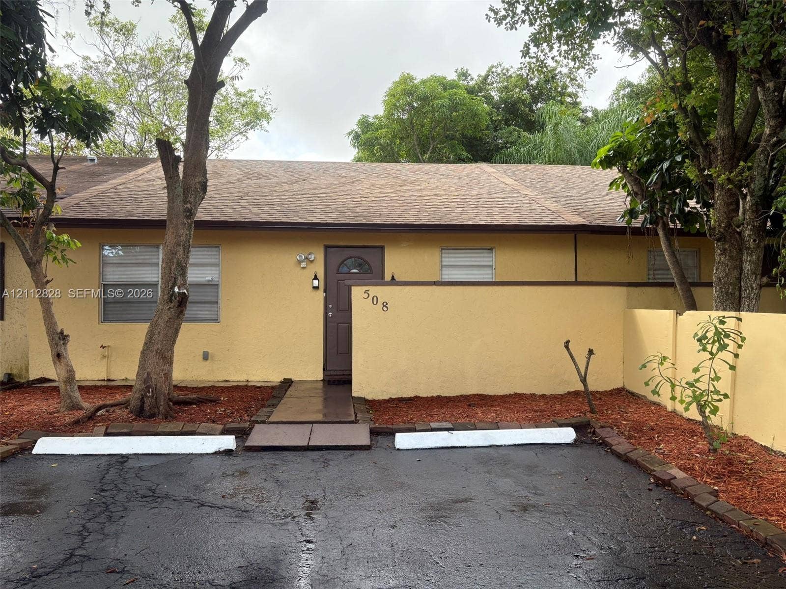 508 NW 43rd Place, Deerfield Beach, FL 33064 Single-story residence featuring a textured exterior, shingled roof, solid entry door, privacy wall, and paved surface parking
