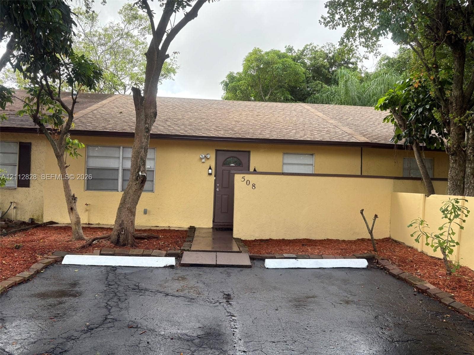 508 NW 43rd Place, Deerfield Beach, FL 33064 Stucco exterior featuring a paved parking area with dual wheel stops, a walkway to the front entry, and masonry privacy wall