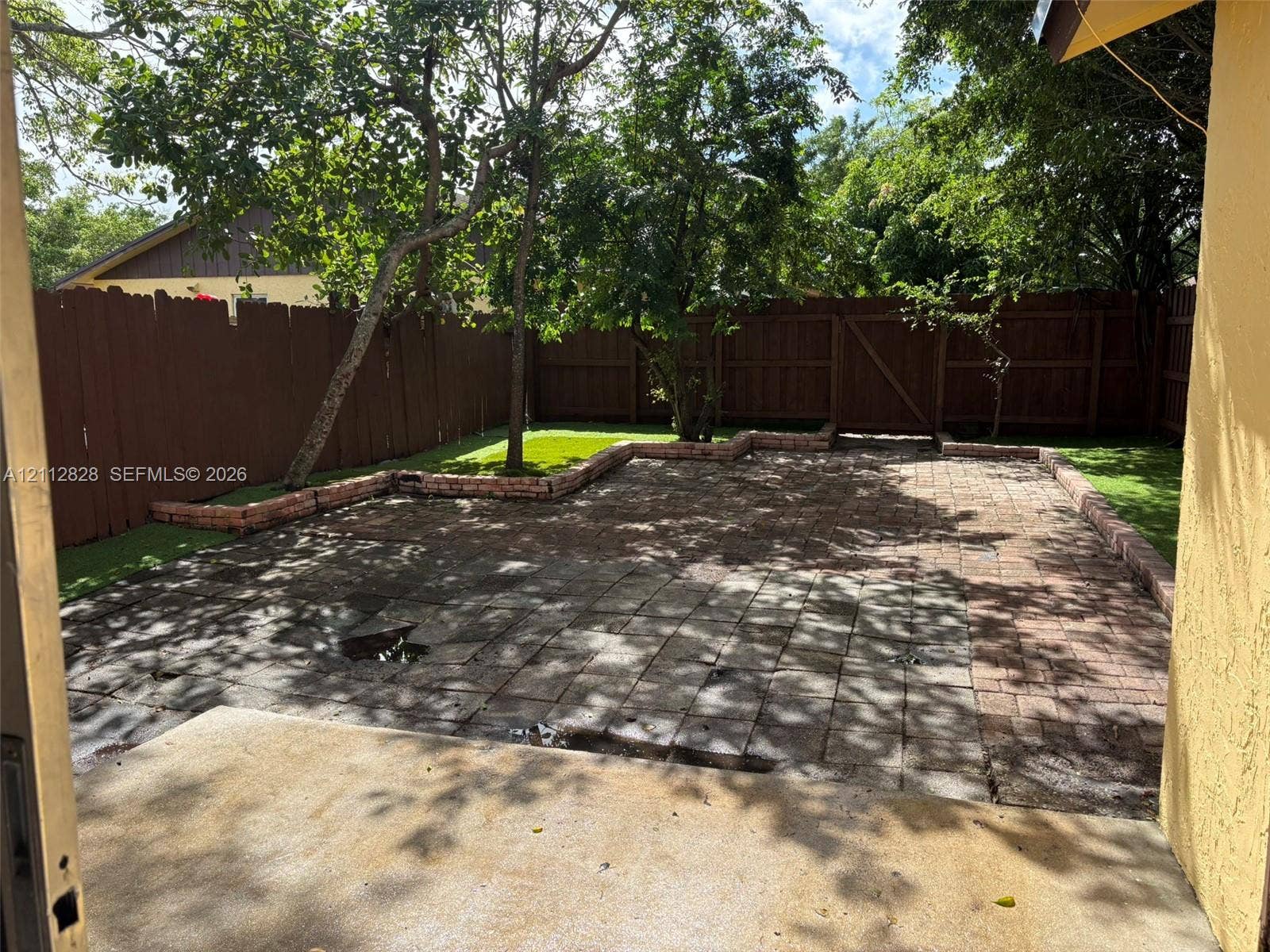 508 NW 43rd Place, Deerfield Beach, FL 33064 Backyard featuring a paved brick patio, raised masonry garden edging, and a wood privacy fence