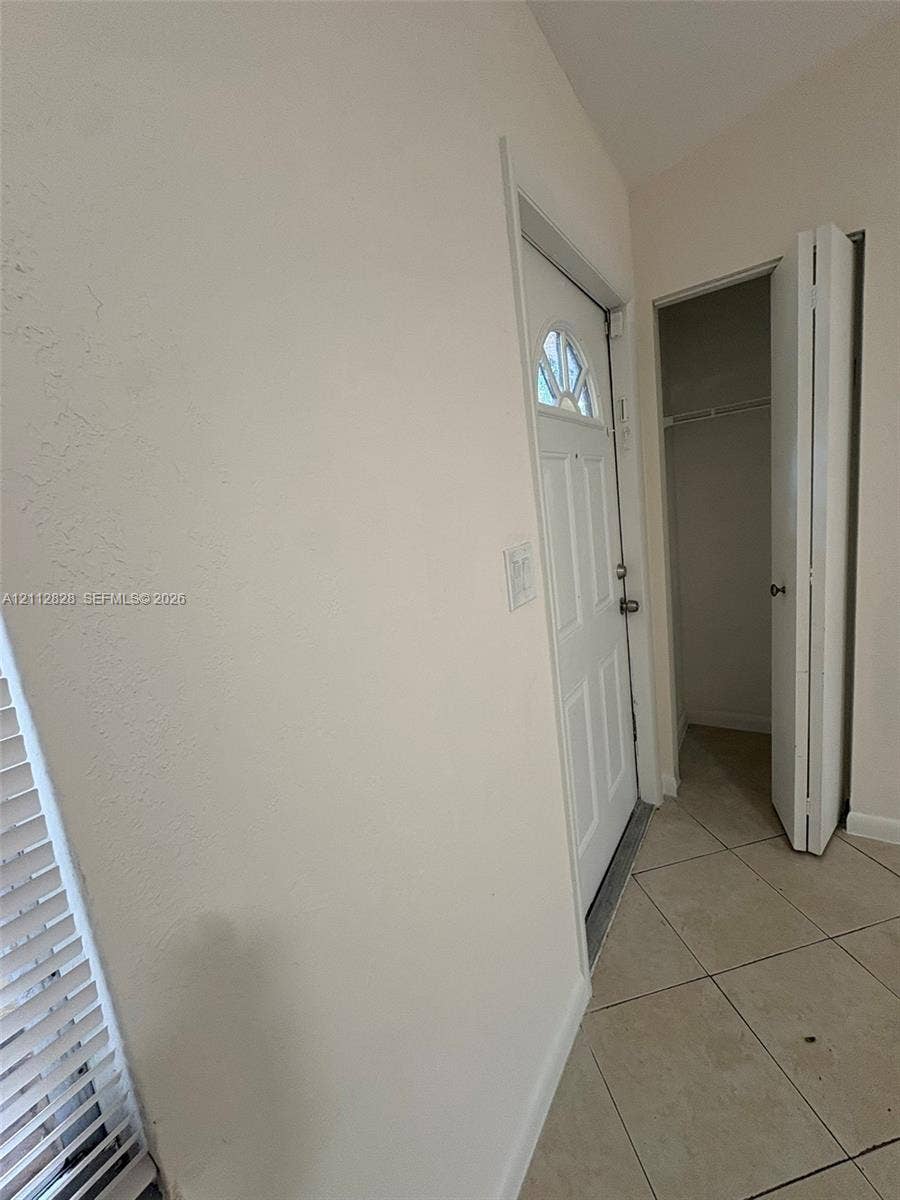 508 NW 43rd Place, Deerfield Beach, FL 33064 Entryway featuring tile flooring, a paneled door with an arched window inlay, and a built-in closet with folding doors
