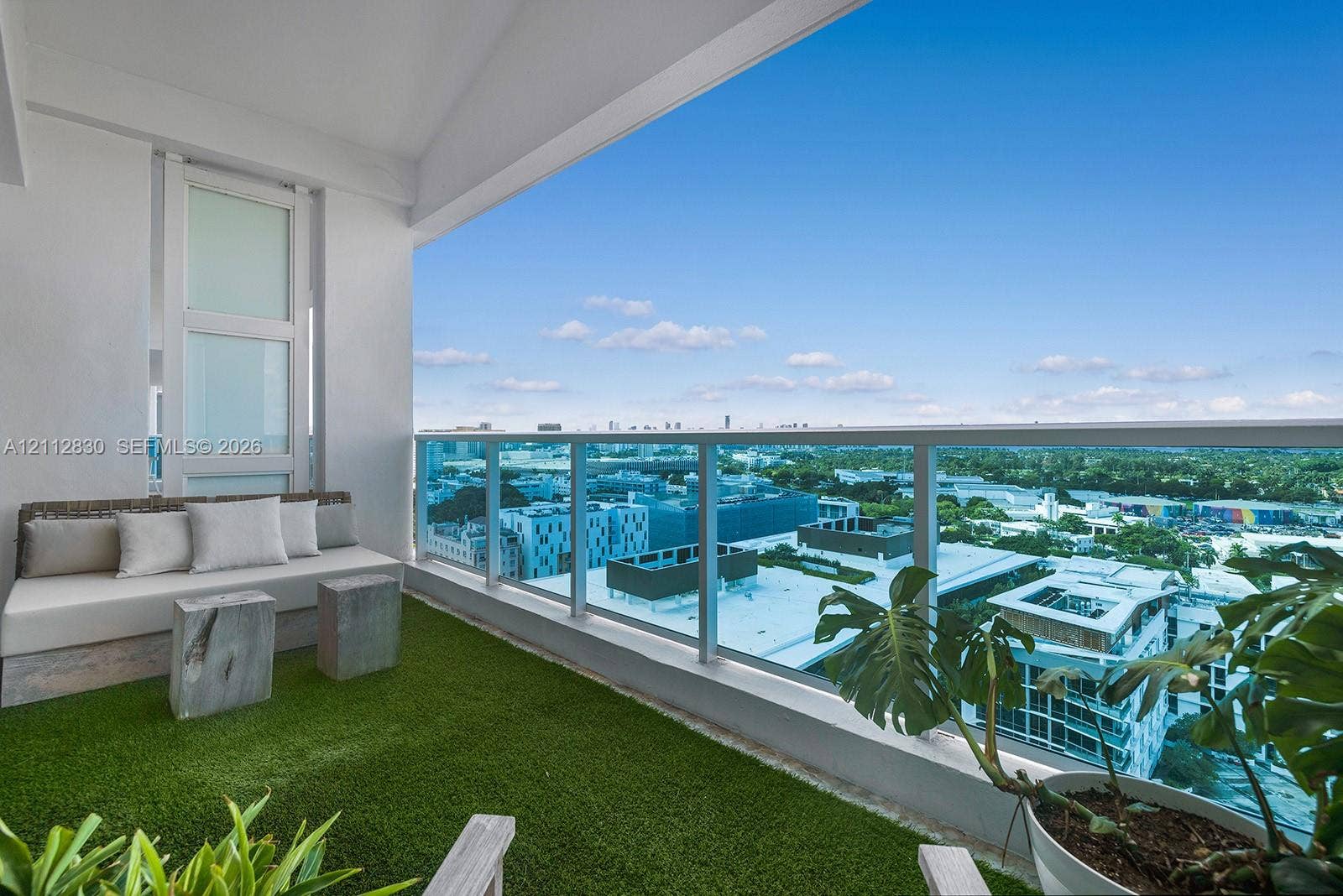 Covered balcony featuring synthetic turf flooring and a glass railing with metal framing
