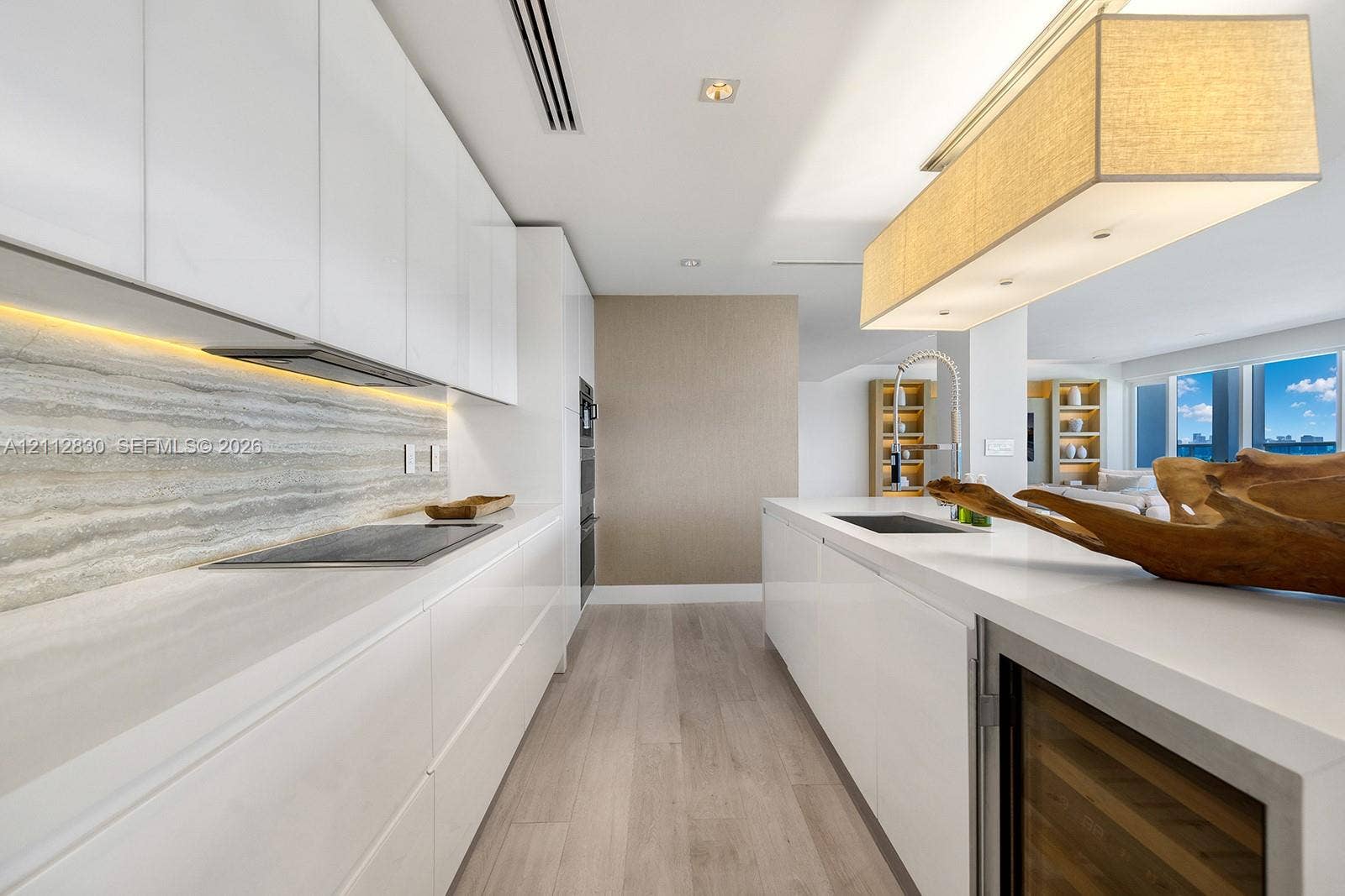 Kitchen featuring high-gloss cabinetry, stone-finish backsplash with integrated under-cabinet lighting, solid-surface countertops, wood-finish flooring, and a built-in wine cooler