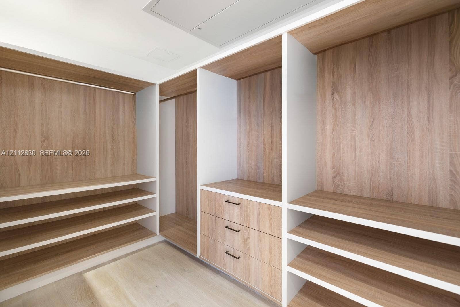 Custom walk-in closet featuring wood-finish cabinetry, built-in shelving, integrated hanging rods, and a three-drawer storage unit with matte black hardware