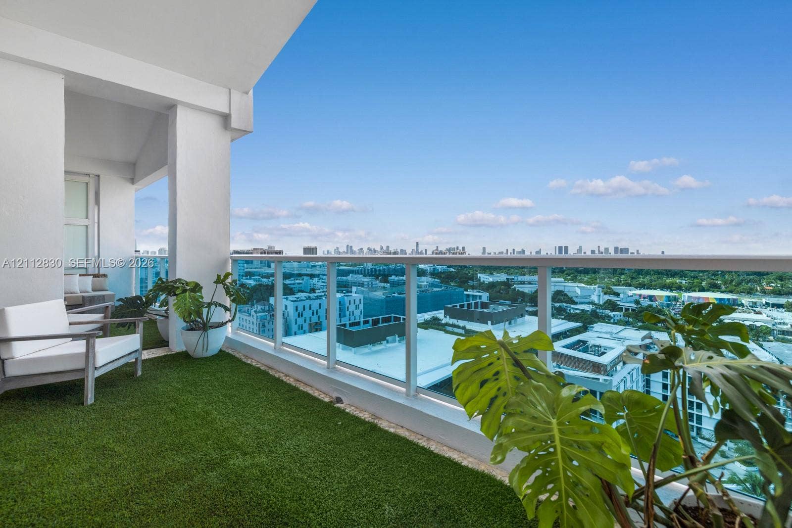 Covered balcony featuring synthetic turf flooring and a glass panel railing