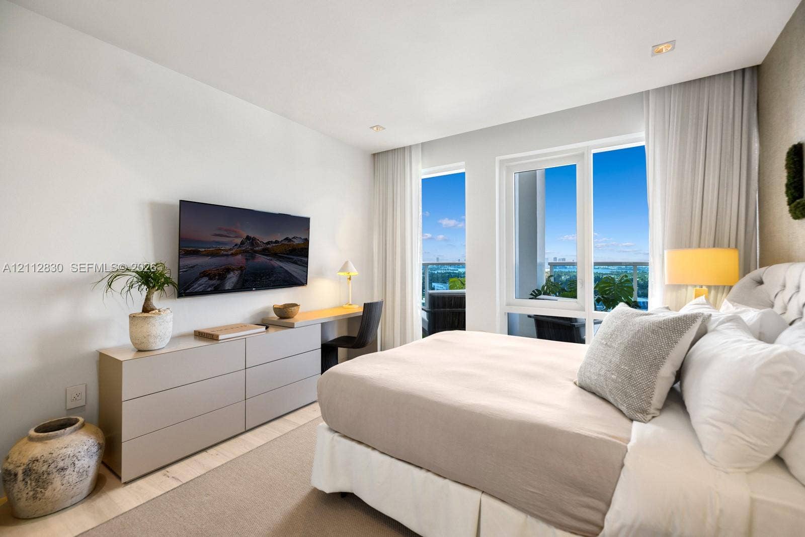 Bedroom featuring wood-finish flooring, built-in desk cabinetry, floor-to-ceiling windows, and balcony access