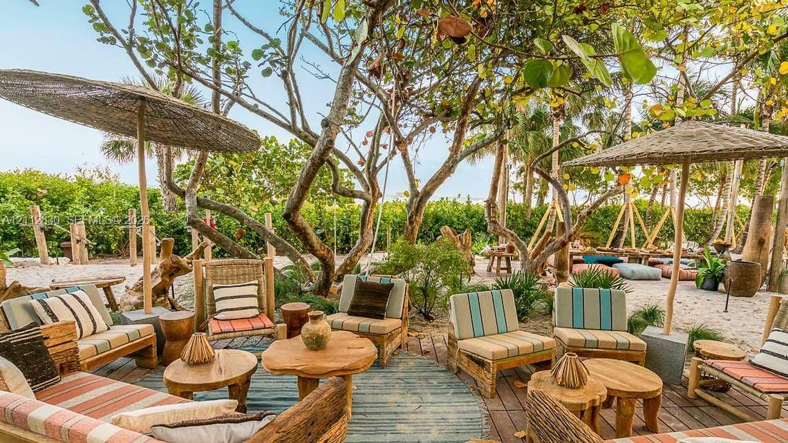 Outdoor lounge area featuring wood decking, sand surfacing, natural-finish wood elements, mature trees, and fixed thatched-roof structures