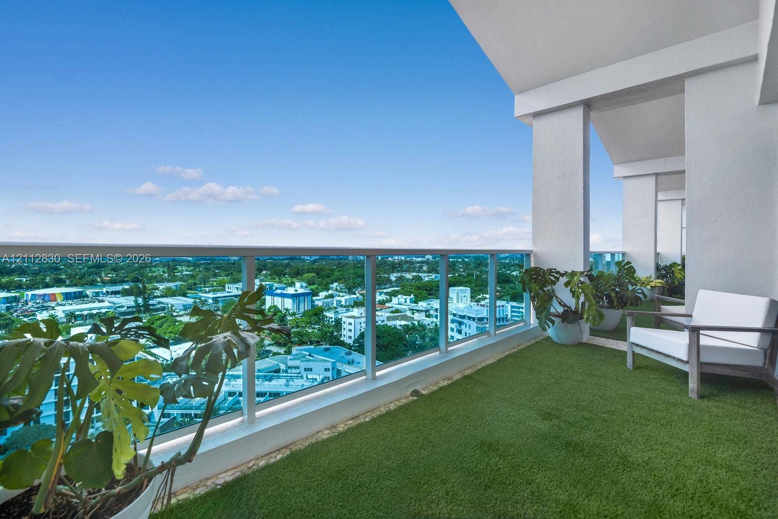 Covered private balcony featuring synthetic turf flooring and a glass panel railing