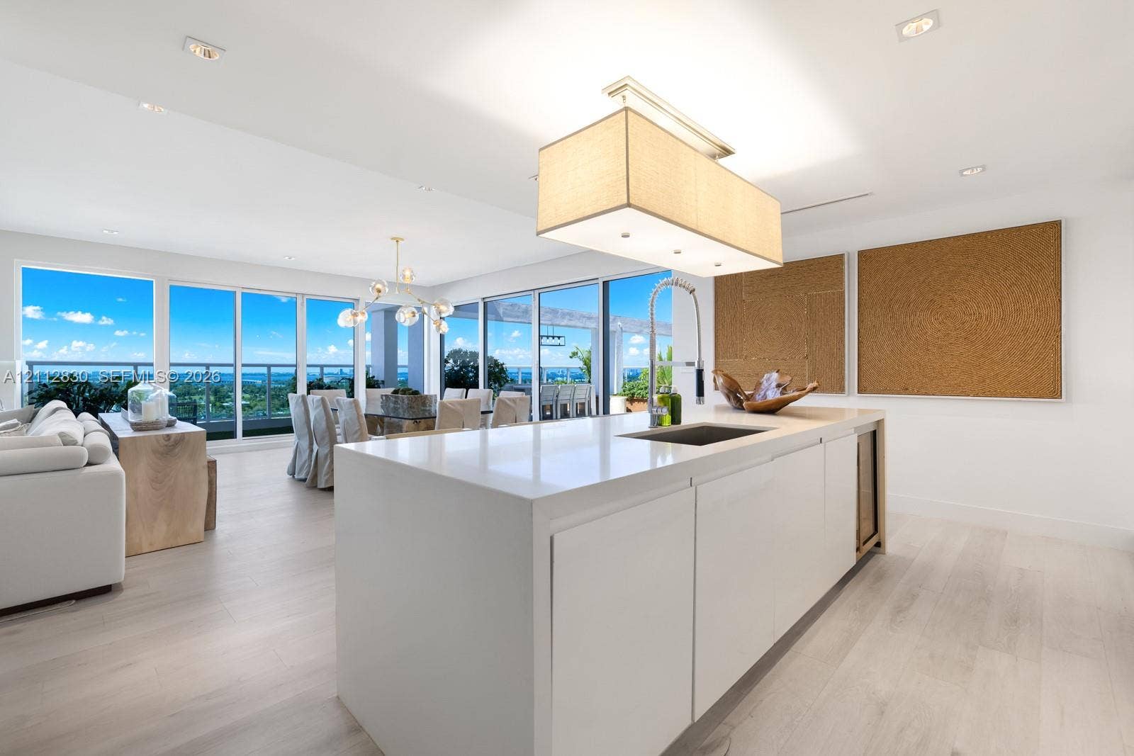 Kitchen island with stone-finish countertop, integrated sink, and built-in under-counter beverage chiller, complemented by wood-finish flooring, recessed lighting, and floor-to-ceiling glass paneling