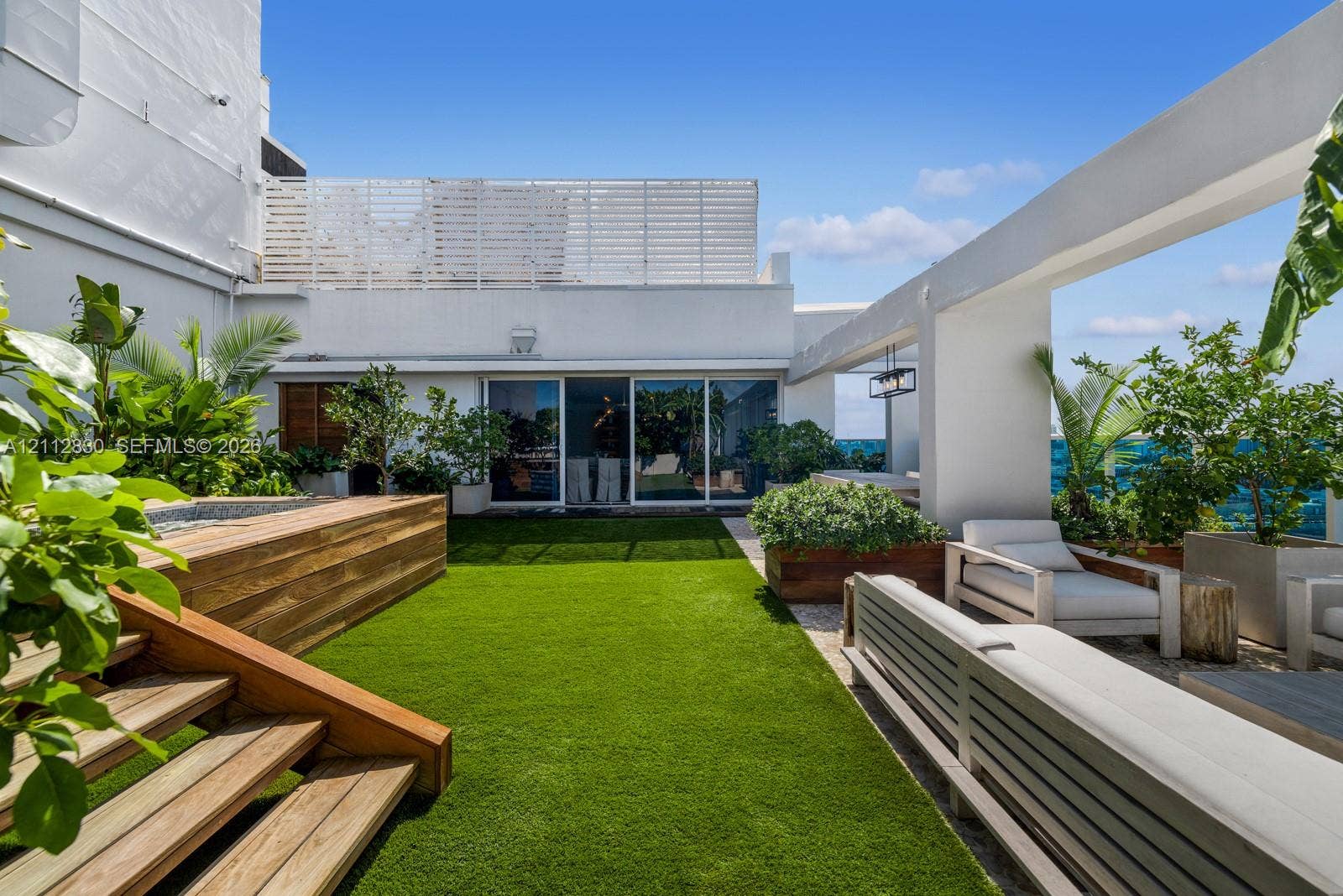 Rooftop terrace featuring artificial turf, tiered wood-finish stairs, a recessed spa, a pergola structure, and built-in wood-finish planters