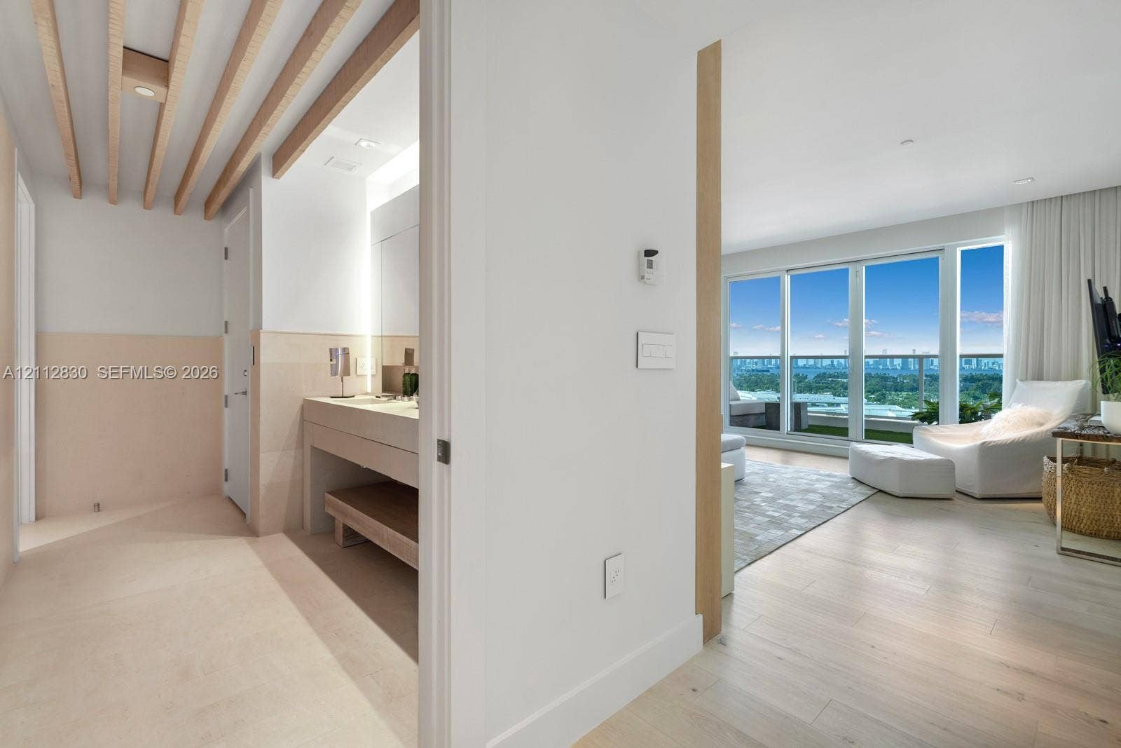 Light-filled interior featuring floor-to-ceiling windows, wood-finish flooring, exposed ceiling beams, a built-in vanity with under-counter shelving, and a balcony with a glass railing
