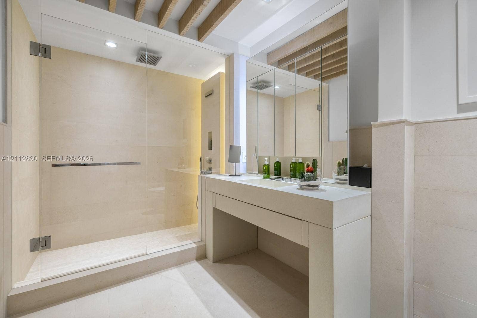 Stone-tiled shower featuring a frameless glass enclosure and rainfall showerhead, complemented by a custom stone vanity with an integrated sink and recessed ceiling beams